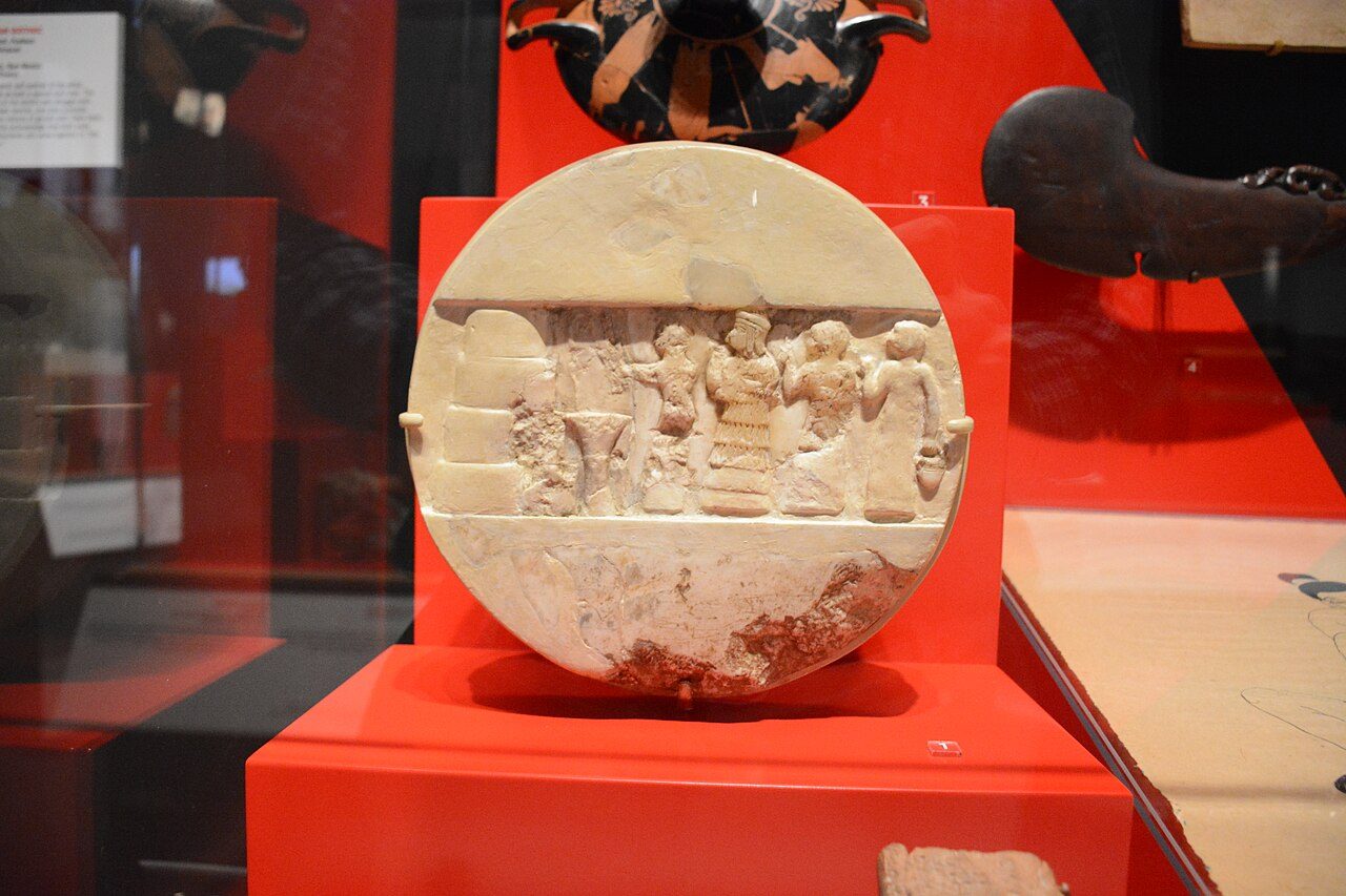A round carved stone disk showing a robed figure at an altar