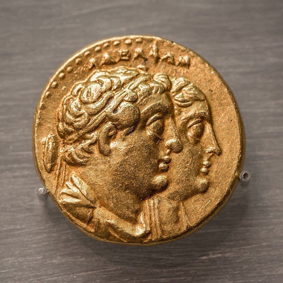 A gold coin with busts of two deified royal couples.